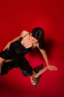 Şık, siyah elbiseli sofistike bir genç kadın ışıl ışıl kırmızı bir arka planla yansımasına bakıyor..