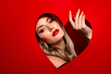 Şık bir kadın modelin portresi, kırmızı rujlu ve sarı dalgalı saçlı, kalp şeklinde bir arka planda cesur bir güzellik..