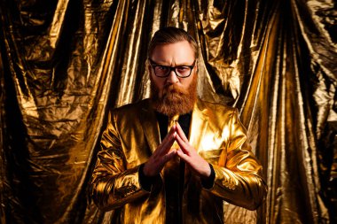 Altın takım elbiseli, kırmızı saçlı karizmatik bir adam, arkaplanda parıldayan bir poz veriyor, zarafet ve bayram cazibesine bürünüyor, festival reklamları ve kutlamalar için ideal..