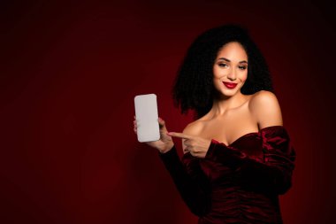 Göz kamaştırıcı şık kız akıllı telefon parmağıyla işaret ediyor. Reklamlar arka planda kadife elbise giyiyor..