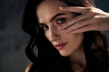 Göz kamaştırıcı bir kızın fotoğrafı. Gri arkaplan üzerinde yüz derisine dokunmak, göz sıkılaştırma prosedürü..