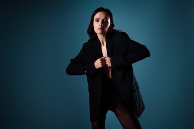 Modaya uygun genç bir kadın, mavi bir arka planı olan siyah bir ceketle poz veriyor, özgüven ve zarafet saçıyor. Güzellik, tarz ve lüks kavramları için ideal..