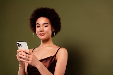 Muhteşem, oldukça çekici, zengin bir bayanın, haki renkli arka planda izole edilmiş modern bir cihazın reklamını yaptığı fotoğraf..