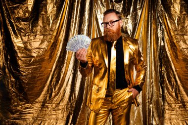 Altın zemine karşı parası olan karizmatik bir adam zarafet ve zenginlik saçan parlak altın bir takım elbise ve şık gözlükler takıyor..