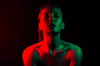 Karanlık bir atmosferde neon kırmızı ve yeşil ışıklı genç bir kadının sanatsal portresi, gösteriş tarzı, güzellik ve moda zarafeti..