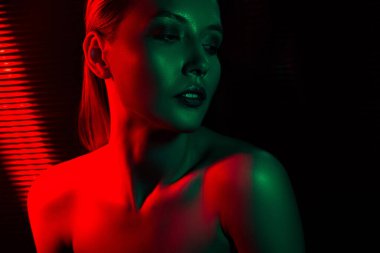 Kontrastlı yeşil ve kırmızı neon ışıklarla aydınlatılmış zarif ve şık bir atmosfer portresi oluşturan güzel bir genç kadına yakın durun..
