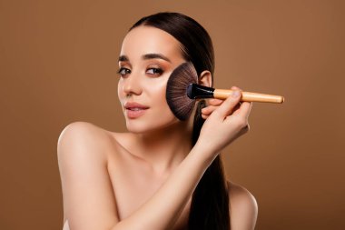 Göz kamaştırıcı güzel bayan model bej rengi arka planda izole edilmiş dekoratif kozmetik allık temel tonu uyguluyor..