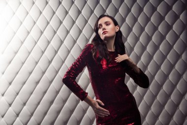 Zarif kırmızı pullu bir elbise içindeki zarif genç bayan beyaz desenli bir arka plana karşı, güzelliği ve şenlikli cazibeyi yansıtıyor.