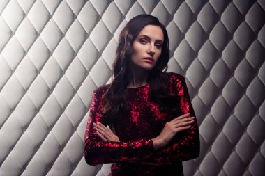 Kırmızı parlayan pullu elbiseli, kendine güvenen genç esmer kadın zarif, zarif ve alımlı beyaz bir arka plana karşı şık bir şekilde duruyor..