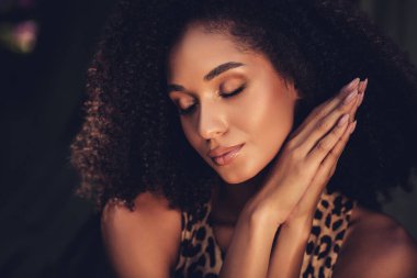 Kıvırcık saçlı, doğal güzelliğini gün ışığında sergileyen genç bir kadının huzurlu ifadesini yansıtan yakın plan bir portre..