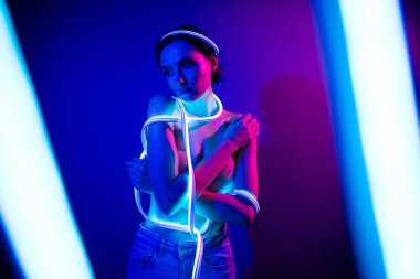 Koyu mavi bir stüdyo ortamında parlayan neon ışıkları olan şık bir genç kadın modern güzelliği ve zarafeti fütüristik bir bükülmeyle yakalıyor..