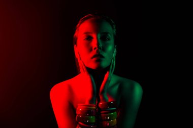 Kırmızı ve yeşil renkli neon ışıklar, bu atmosferik ve modaya uygun stüdyo resminde koyu arkaplanı olan şık genç bir kadını ön plana çıkarıyor..