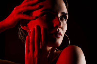 Çekici, genç bir kadının fotoğrafı. Yüze dokunuyor. Ten rengi kırmızı, omuzları siyah renkli..