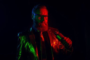 Parlak takım elbiseli, parlak neon ışıklarla aydınlatılmış, bakımlı sakallı, karizmatik bir adam. Elinde bir mikrofon tutarken, eski ve klasik zarafeti yansıtırken entelektüellik saçıyor..