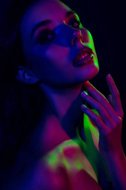 Neon mavisi ve yeşil ışıkla aydınlatılmış koyu bir estetik güzelliği ve zarafeti olan genç bir kadının etkileyici ve cesur görüntüsü..