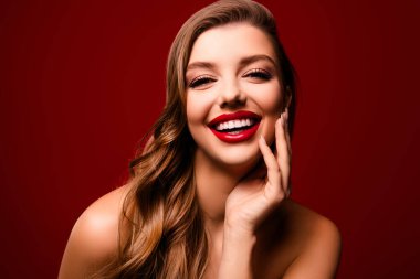 Mutlu gülümseyen kadının yüzü dokunuyor. Kırmızı arka planda parlak ruj izi olan pürüzsüz tenin tadını çıkarıyor..