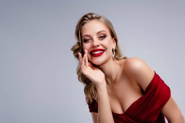 Kırmızı elbiseli, neşeli gülümseyen kadın gri arka planda el ele tutuşup sohbet ediyor..