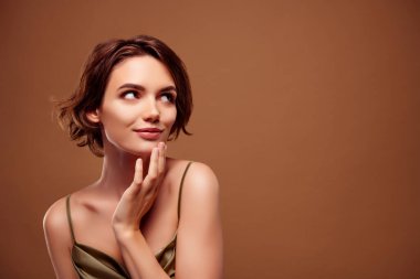 Çekici genç bir kadının fotoğrafı boş görünüyor. Kahverengi arka planda izole edilmiş şık haki rengi kıyafetler giyiyor..