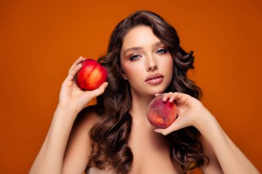 Kıvırcık saçlı, elinde şeftali olan güzel bir esmer. Canlı turuncu arka plan zarafet ve cazibeyi arttırır. Promosyonlar için şehvet, moda ve güzelliği çağrıştırıyor..