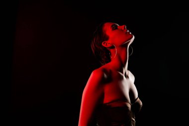 Çekici, seksi, şehvetli, siyah arka planda neon ışık saçan, modaya uygun giyinen genç bir kadının fotoğrafı..