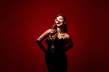 Kırmızı arka planda kuş tüyü bir elbise giyerek gülümseyen zarif bir bayanın fotoğrafı..