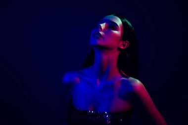 Canlı neon ışıkları altında modellik yapan, karanlık ve modaya uygun bir ortamda güzelliğini, cazibesini ve çekiciliğini sergileyen, gece hayatı ve modern moda ile yankılanan şık genç bir kadın..