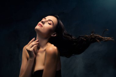 Parlak tenli, esmer, genç bir kadının yakın plan portresi dramatik bir karanlık arka plana karşı doğal güzelliğini ve tarzını sergiliyor..