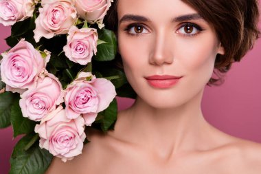 Güzel bir hanımefendinin, çiçek açan gül tomurcuklarının yanında pembe arkaplanda zarif bir makyaj yaparken yakın plan fotoğrafı..