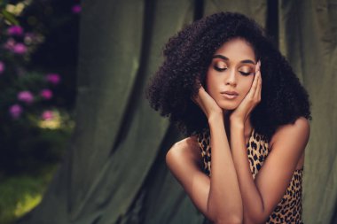 Güzel genç bir kadın huzurlu bir bahçede doğanın tadını çıkarıyor, şık görünüşü kendine güven ve cazibe yayıyor, canlı bir çevreyle harmanlanıyor..