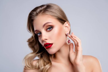 Göz kamaştırıcı bayan, kameraya bakıyor. Küpelere dokunuyor. Gri arka planda değerli mücevherlerin reklamını yapıyor..