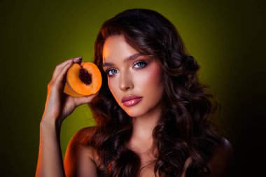 Büyüleyici bir görüntü, olgun bir şeftali tutan, koyu yeşil bir ortamda güzel ve sofistike bir kadın..