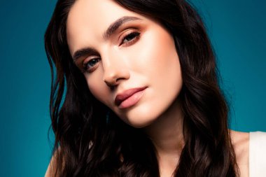 Güzel ve zarif bir genç kadının yakın plan portresi kusursuz makyajlı ve esmer saçlı, mavi bir arkaplanda izole edilmiş..