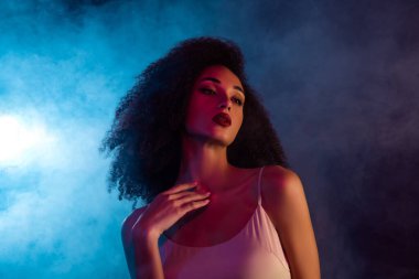 Şık bir kadın, canlı, neon ışıklı bir arka plana karşı, zarafet ve modern güzelliği somutlaştırarak, özgüvenle poz verir. Cazibe ve entellektüellikle dolu, çarpıcı aydınlatmayla vurgulanmış bir ortam..