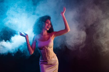 Zarif genç bir kadın zarif bir şekilde dans ediyor. Etrafı renkli dumanlı neon ışıklarla çevrili. Modaya uygun bir elbise içinde..