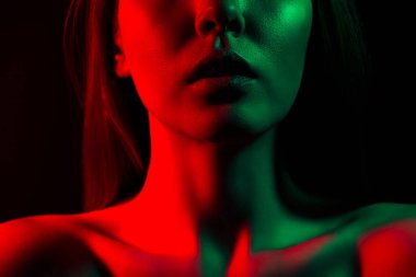 Kırmızı ve yeşil neon ışıkla aydınlatılmış, koyu, gizemli bir arka plana karşı şık ve dramatik bir atmosfer yaratan genç bir kadının yakın çekim sanatsal fotoğrafı..