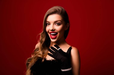 Şok olmuş kahverengi kıvırcık saçlı kadın dokunmatik göğsünün fotoğrafı kırmızı arka planda giyilen elbiseyi hisset..