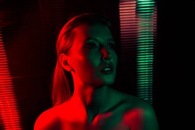 Kırmızı ve yeşil neon ışıklarla aydınlatılmış genç bir kadının portresi, canlı renkler, sanatsal ifade, gece hayatı ve stil atmosferi.