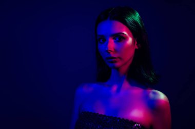 Renkli neon ışıklarla aydınlatılmış büyüleyici bir kadının büyüleyici portresi, büyüleyici bir cazibe, entelektüellik ve kendini ifade eden bir duygu, onun cazibesini vurgulayan koyu mavi bir arka plan..