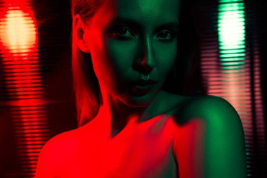 Yoğun kırmızı ve yeşil neon ışıkla aydınlatılan genç bir kadın dramatik ve şık bir atmosfer yaratarak güzelliğini ve modern modasını ön plana çıkarıyor..