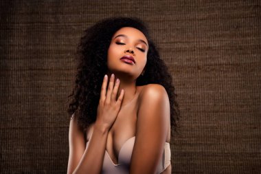 Tarz sahibi, kıvırcık saçlı ve zarif bir şekilde kahverengi arka planda poz veren güzel bir kadının samimi stüdyo portresi.