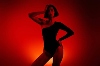 Genç bayan model zarif bir şekilde parlak turuncu bir arka plana poz veriyor, güzelliğini, tarzını ve modern şehvetini vurguluyor..