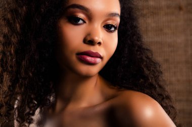 Kıvırcık saçlı, çarpıcı güzelliğini, kusursuz makyajını ve tarafsız bir arkaplana karşı ışıltılı özgüvenini vurgulayan zarif bir yakın plan..