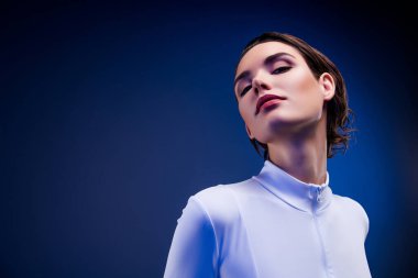 Mükemmel makyaj ve klas tarzıyla modern moda sergileyen genç bir kadının göz kamaştırıcı yakın çekimi, mavi neon ışığıyla aydınlatılıyor..