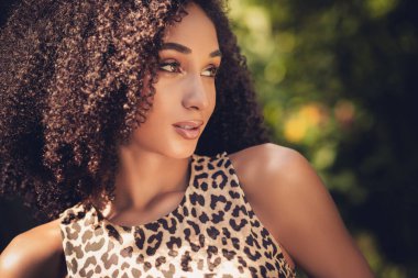 Özgüvenle poz veren şık genç bir kadın, arka planda yeşillik bulanıklaşmışken gün ışığında doğal güzellik ve moda sergiliyor.