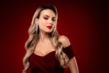 Uzun dalgalı sarı saçlı, şık kırmızı bir elbise giyen zarif bir genç bayan, etkileyici ve sofistike. Koyu bir bordo arka planda, resim şehvet ve cazibe yayar..