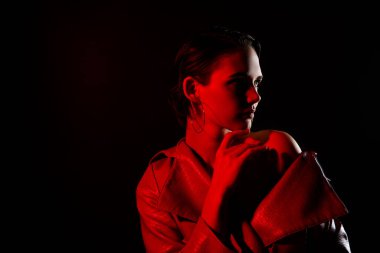 Seksi, genç bir kadının dokunuşunun fotoğrafı. Yumuşak tenli. Boş bir alana bak. Siyah arka planda parlak kırmızı ceketli..