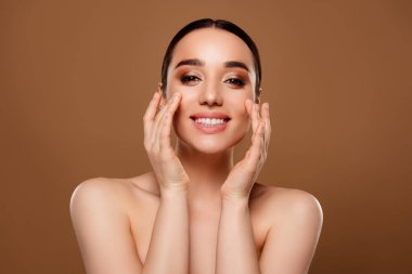 Göz kamaştırıcı mutlu modelin portresi nemlendirici krem sürerek bej rengi arka planda izole edilmiş yüz makyajı..