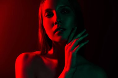 Karanlık bir arka planda neon kırmızı ve yeşil ışıklı genç bir kadının çarpıcı portresi gizem ve şehveti çağrıştırıyor..