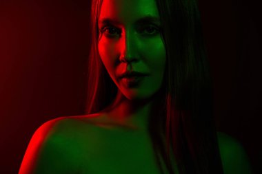 Kırmızı ve yeşil ışıkla aydınlatılmış genç bir kadının yaratıcı portresi. Estetik, zarafet, moda ve modernliğe vurgu yaparken, aydınlatma efektleriyle şehvetli ve atmosferli bir şekilde taşınıyor..