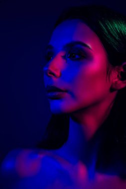 Bir kadının çarpıcı portresi neon mavi ve kırmızı ışıkla aydınlatılıyor, güzelliğini arttırıyor ve koyu bir arka plana karşı zarif ve modaya uygun bir atmosfer yaratıyor..